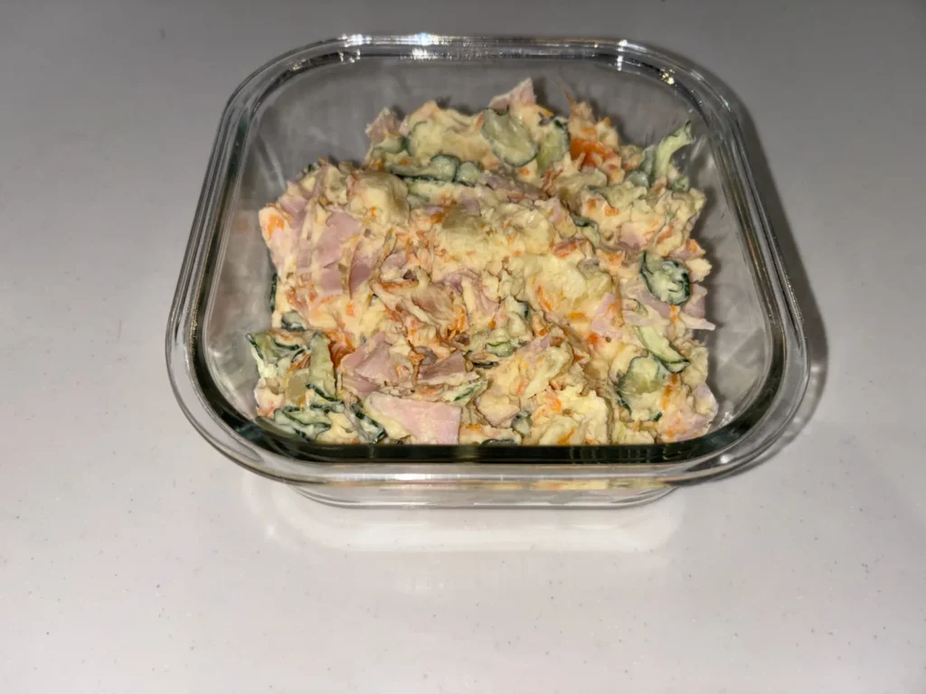 耐熱ガラスの保存容器に詰めたポテトサラダ。ふたを開けた状態で、ハムときゅうりが見えている