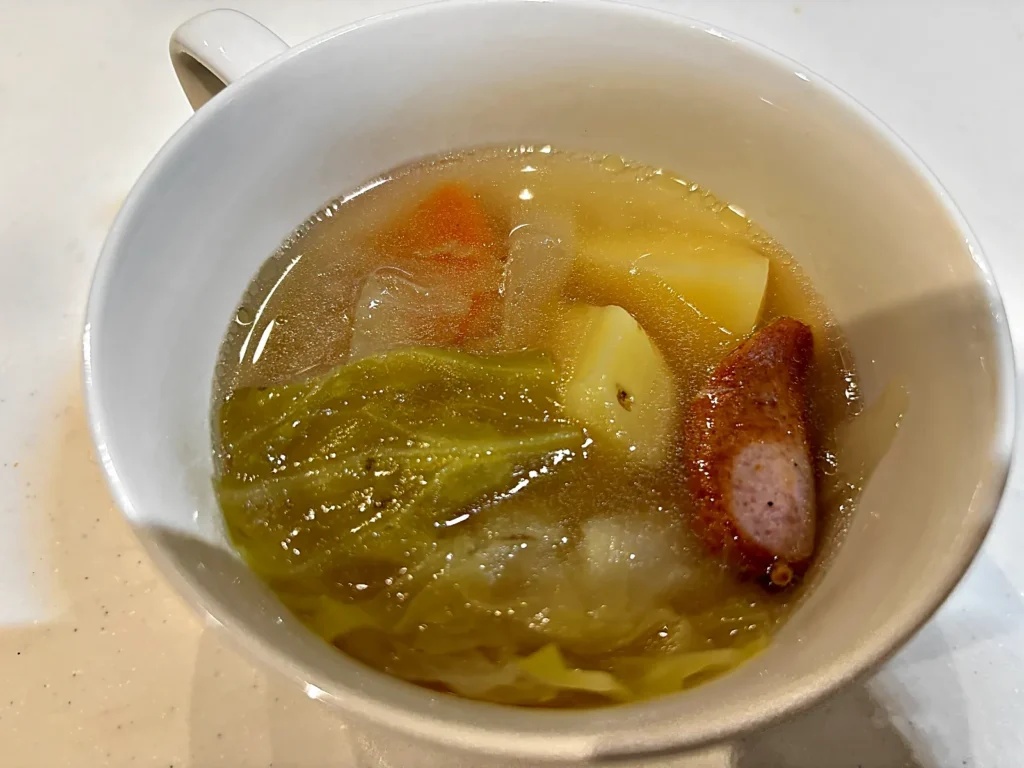 白いスープカップに盛ったポトフ。キャベツ・じゃがいも・にんじん・ウインナーが入っている